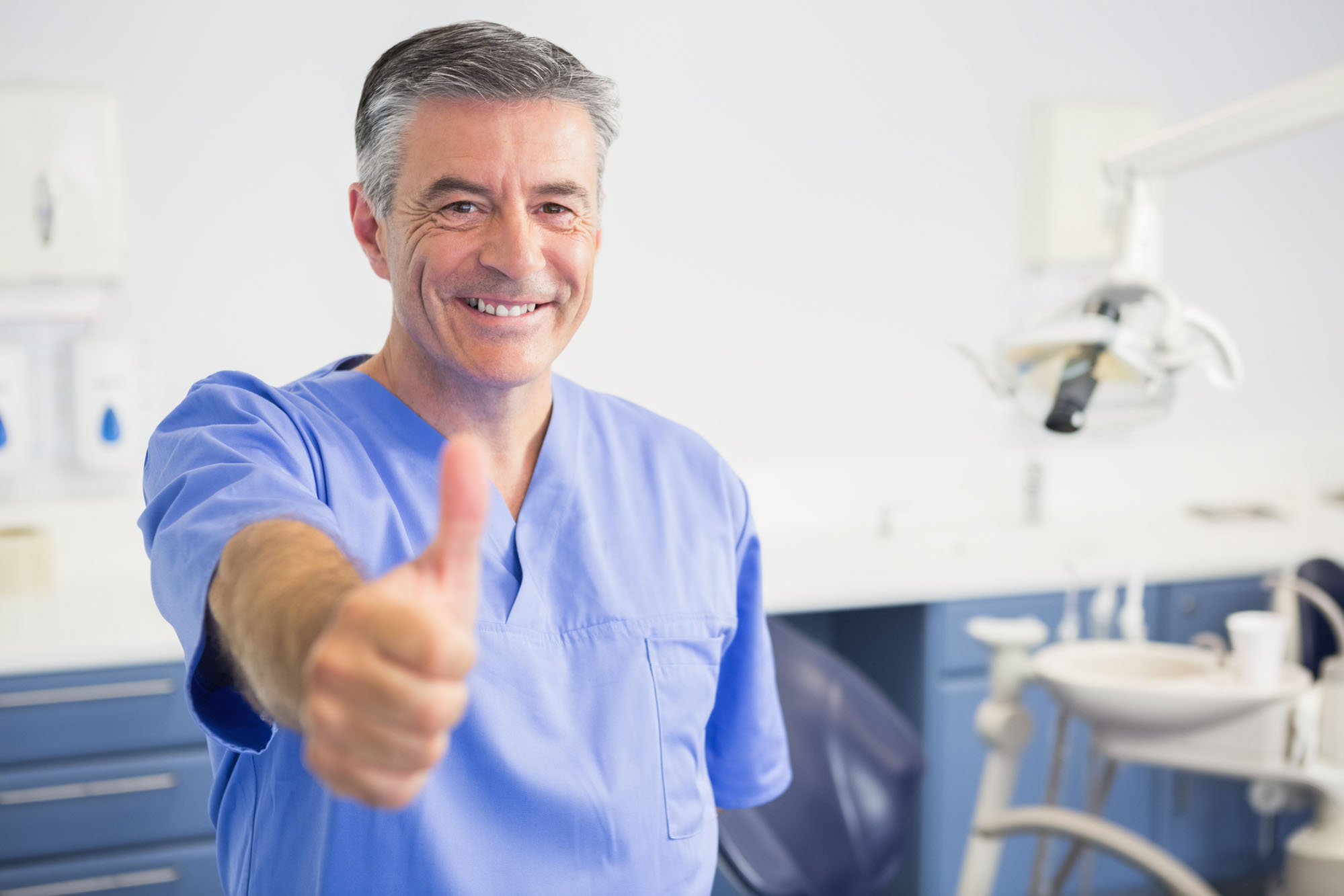 Portrait of happy dentist with thumbs up in dental clinic